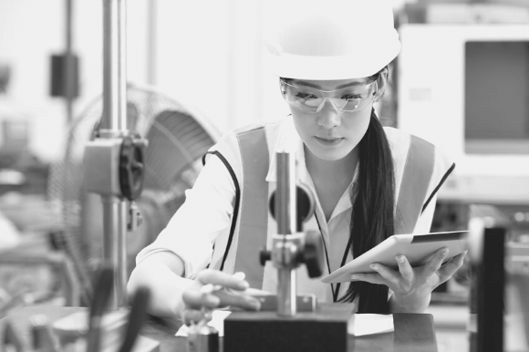 Quality engineer, wearing a hardhat, takes measurements of a part to determine whether it meets the company's standards.