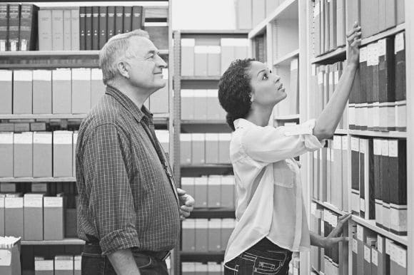 A paraprofessional helps her employee locate a file.