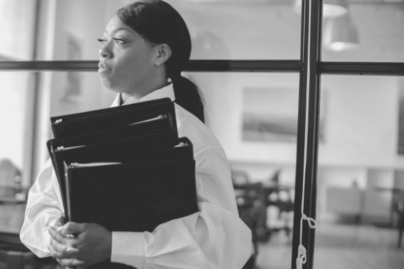 File clerk inside an office, carrying several binders.